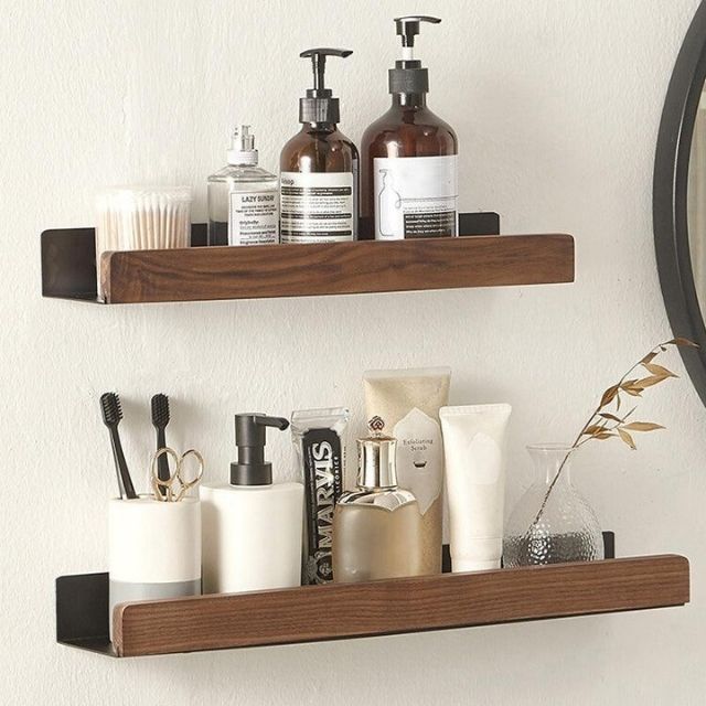 Two dark walnut wood bathroom shelves with black metal brackets holding toiletries, toothbrushes, and decor.