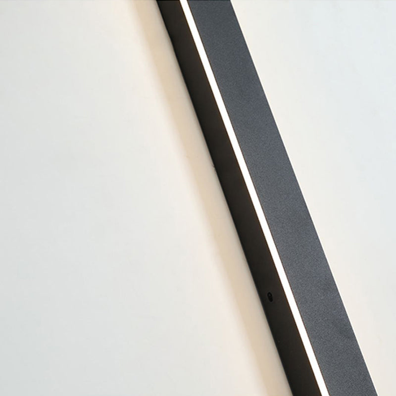 Modern minimalist black linear LED outdoor wall light mounted on a plain white wall, glowing with a soft light.