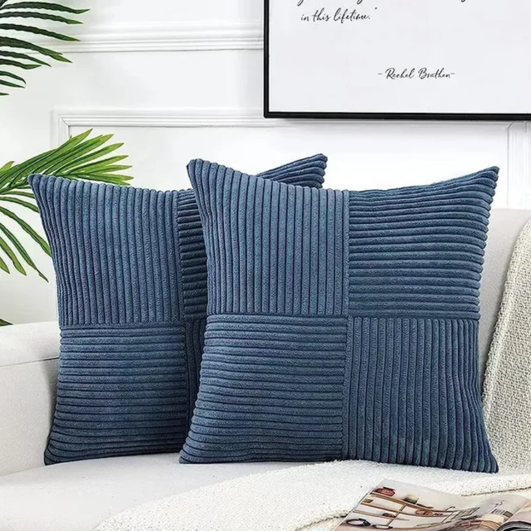 Two square blue corduroy decorative cushions with ribbed patterns, arranged on a white sofa in a bright, modern room.