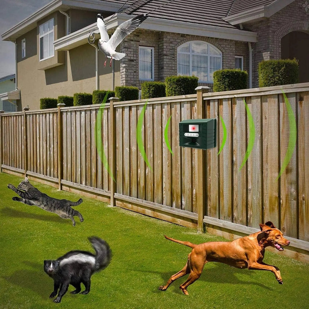 Fitlybuy green ultrasonic repeller mounted on a backyard fence, emitting sonic waves to deter animals from the lawn.
