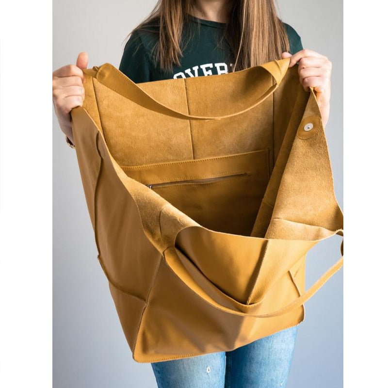 Person holding an oversized, mustard-yellow leather weekender bag with an open top and internal zip pocket.