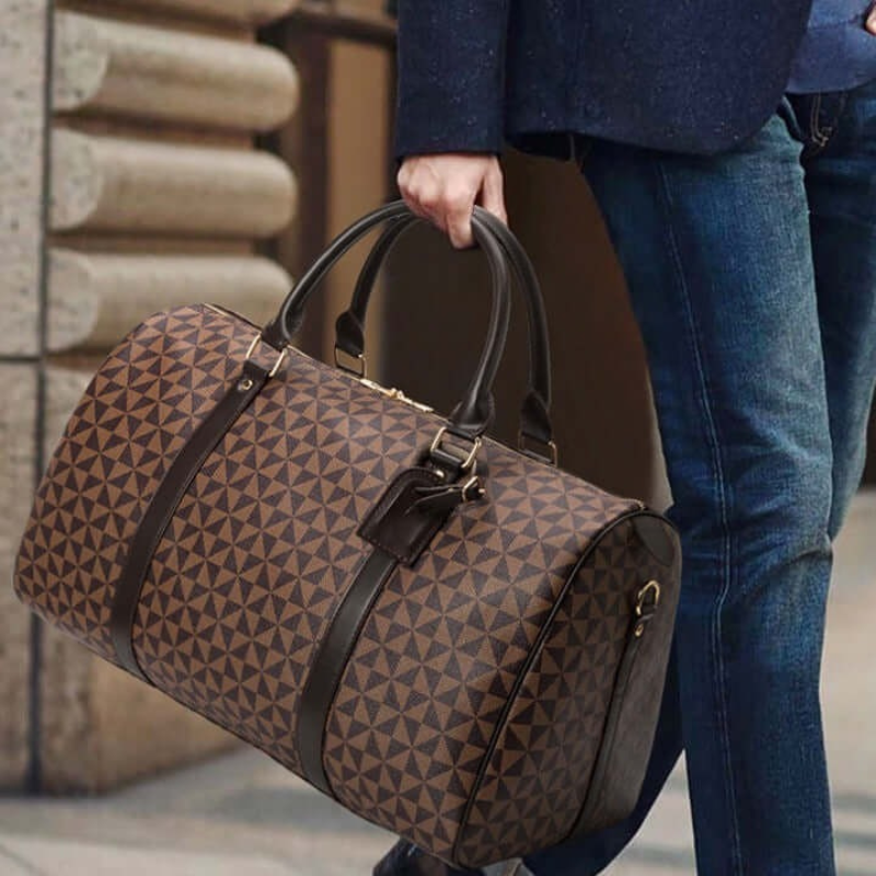 Person carrying a brown, patterned Fitlybuy Westman leather duffle bag with dark leather handles and trim.