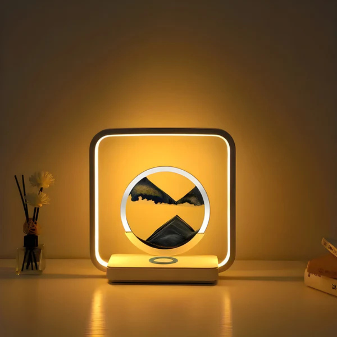 Fitlybuy SandAura square LED lamp with circular flowing sand art, emitting warm light on a desk with decor and books.