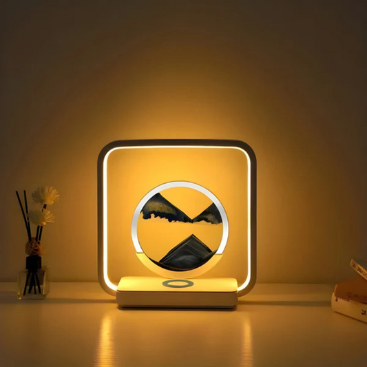 Fitlybuy SandAura square LED lamp with circular flowing sand art, emitting warm light on a desk with decor and books.