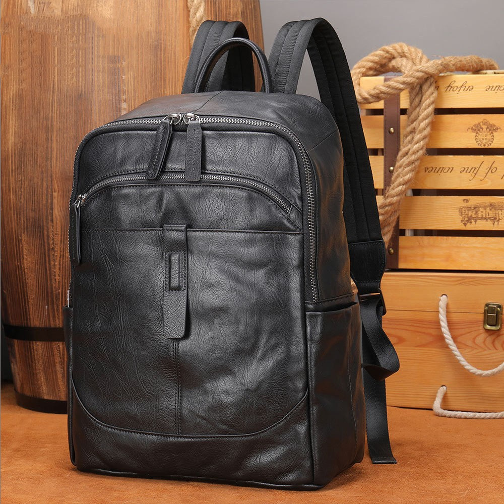 Fitlybuy black leather laptop backpack for 15.6-inch devices, featuring dual zippers and front pocket on rustic table.