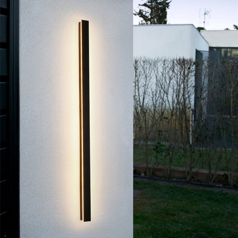 Fitlybuy minimalist black vertical LED outdoor wall light mounted on a white exterior wall at twilight.