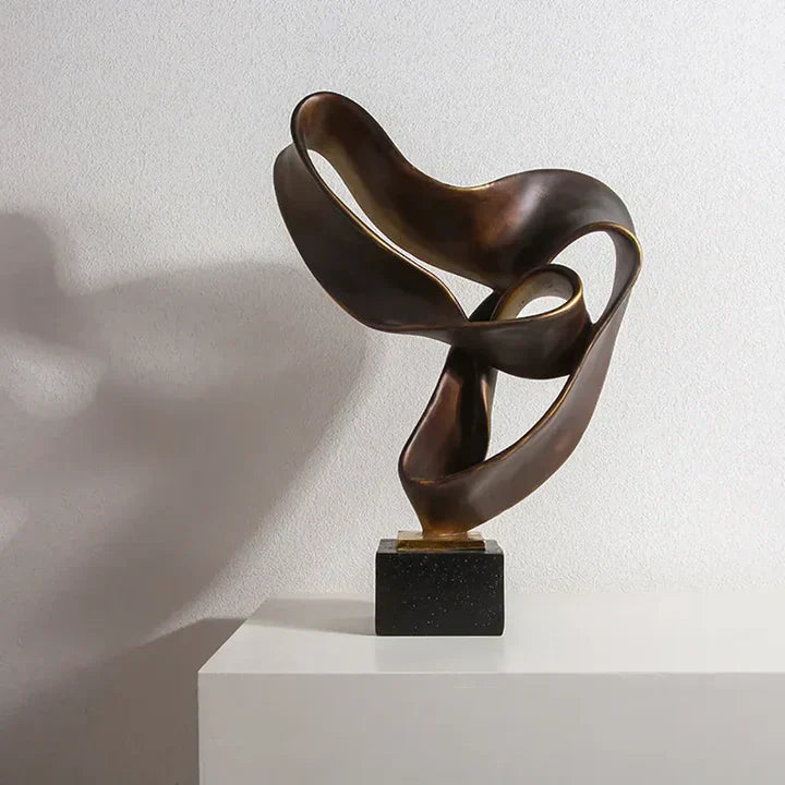 Fitlybuy Vida bronze-colored resin sculpture with a modern, fluid abstract design on a black base against a white wall.