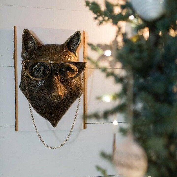 Bronze-colored fox head wall decor wearing glasses with a gold chain, mounted on a rustic white wood board.