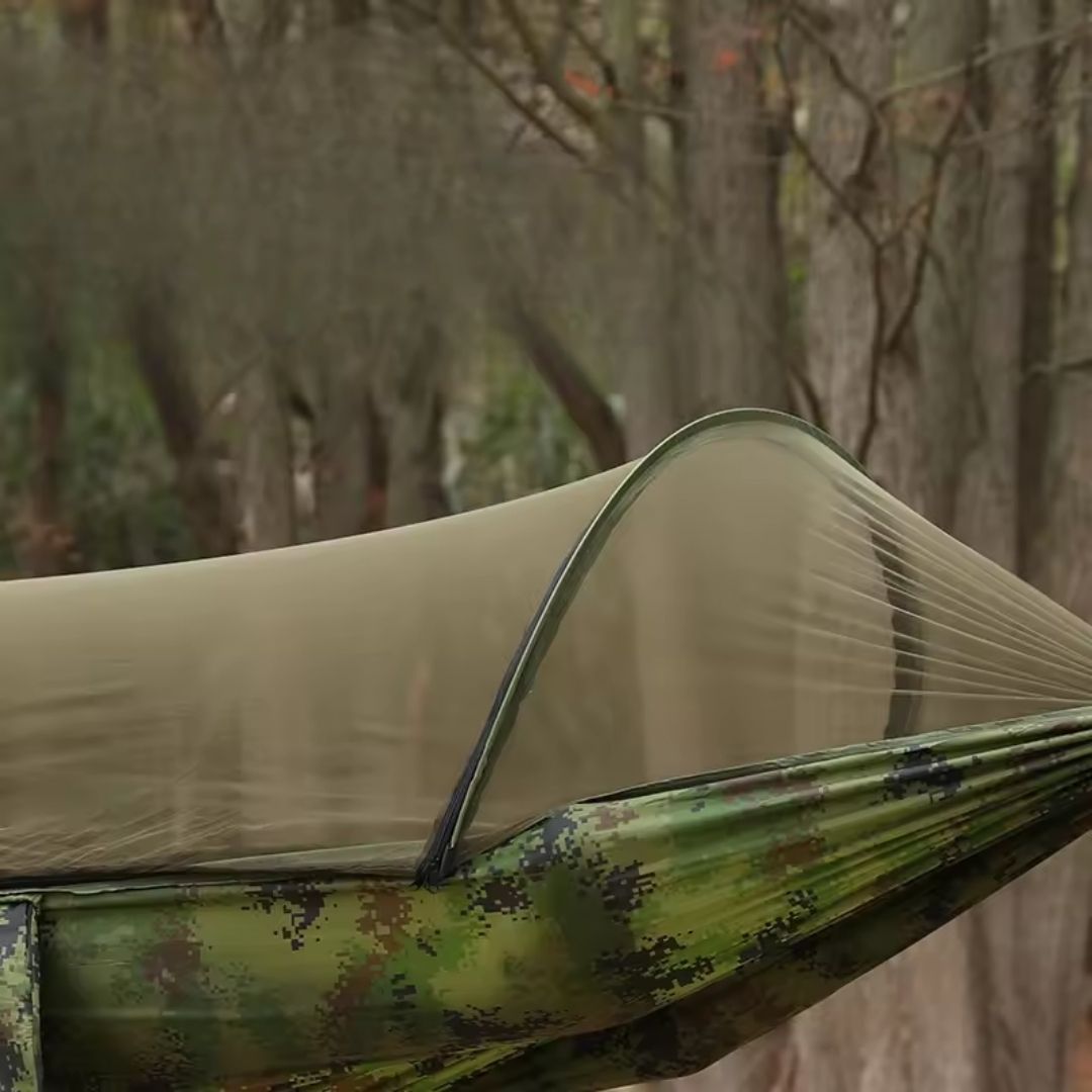 Fitlybuy camo hammock with integrated BugShield mosquito net, set up outdoors among blurred trees.