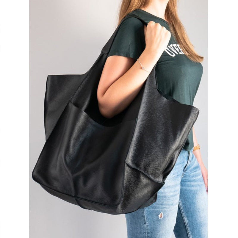 Woman wearing an oversized black leather Fitlybuy weekender bag with a slouchy, spacious design over her shoulder.