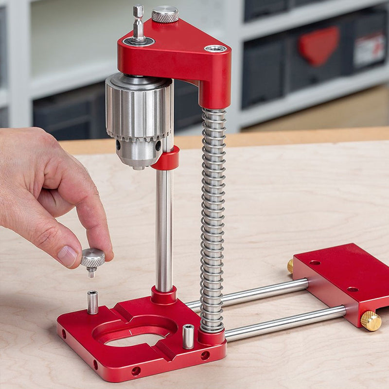 Red Fitlybuy woodworking drill locator with spring-loaded guide, precision metal base, and steel chuck on wood surface.