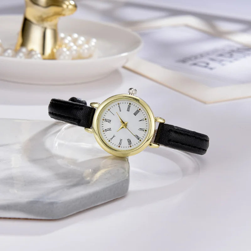 Fitlybuy Billie gold round watch with white face, Roman numerals, and black leather strap on a marble surface.