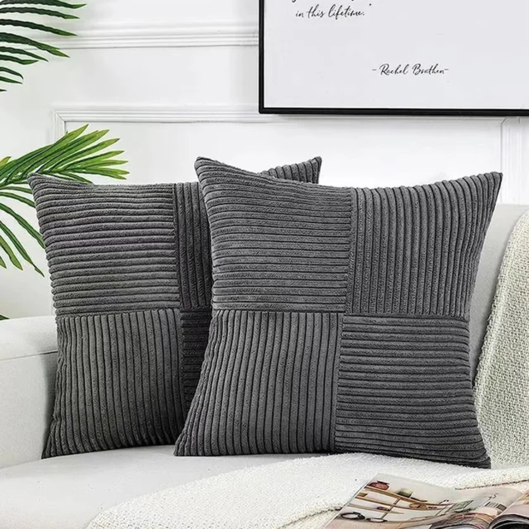 Two dark gray, corduroy-textured square cushions with a vertical and horizontal ribbed pattern on a white couch.