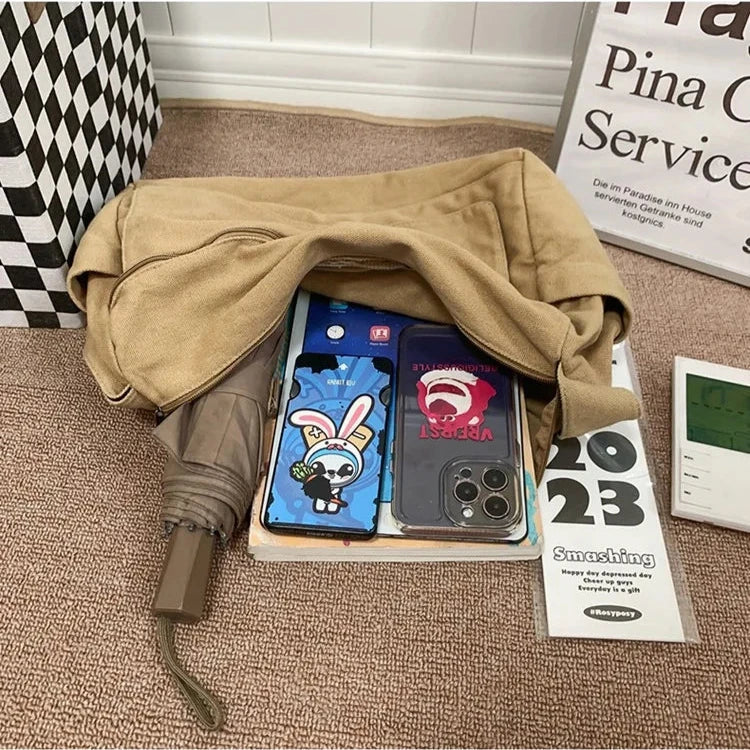 Tan Fitlybuy canvas sling bag containing a tablet, smartphone, umbrella, and notebook on a textured beige surface.
