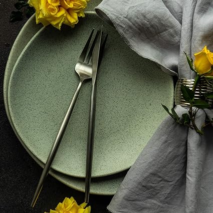 Fitlybuy Torin matte stainless steel fork and knife on speckled green plates with a grey linen napkin and yellow roses.