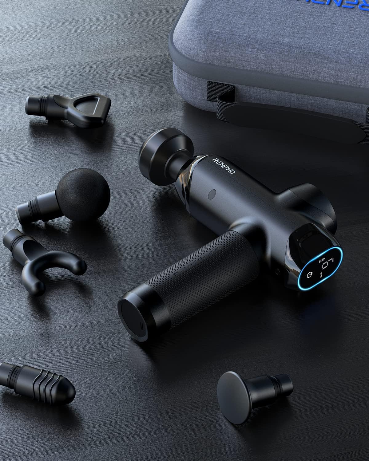 Black handheld massage gun with a digital screen and five interchangeable heads, set on a table with a carrying case.