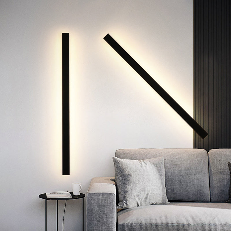 Two modern black minimalist LED linear wall lights glowing against a white wall above a grey sofa.