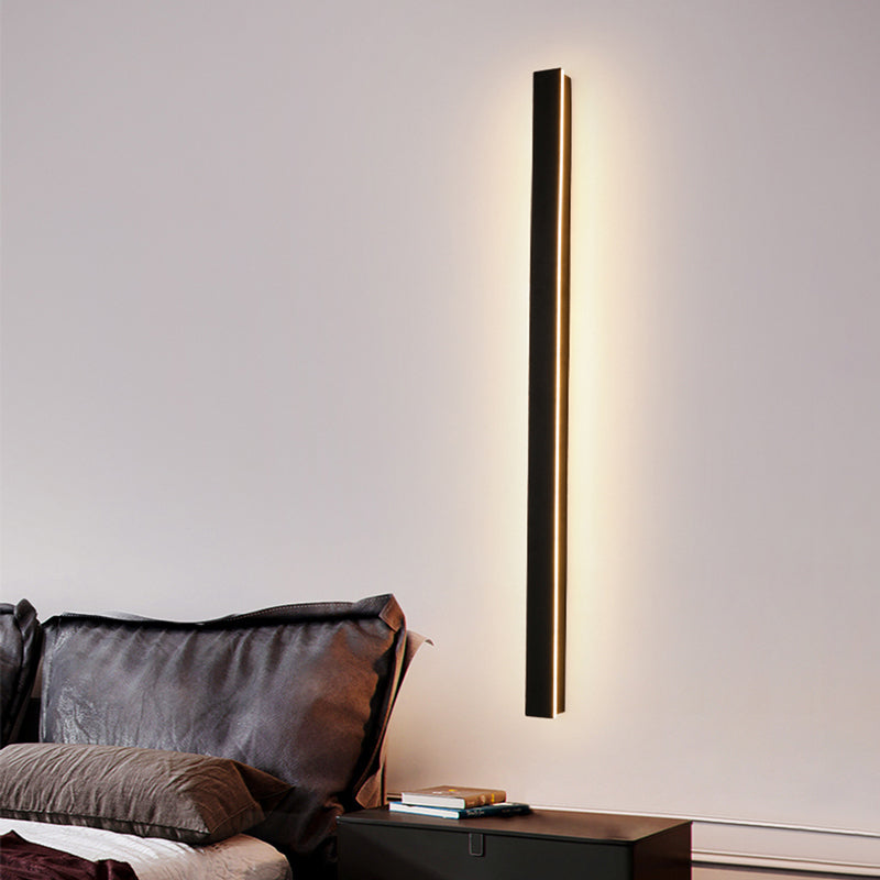 Fitlybuy minimalist black vertical LED wall light mounted on a bedroom wall, casting a soft, warm glow.
