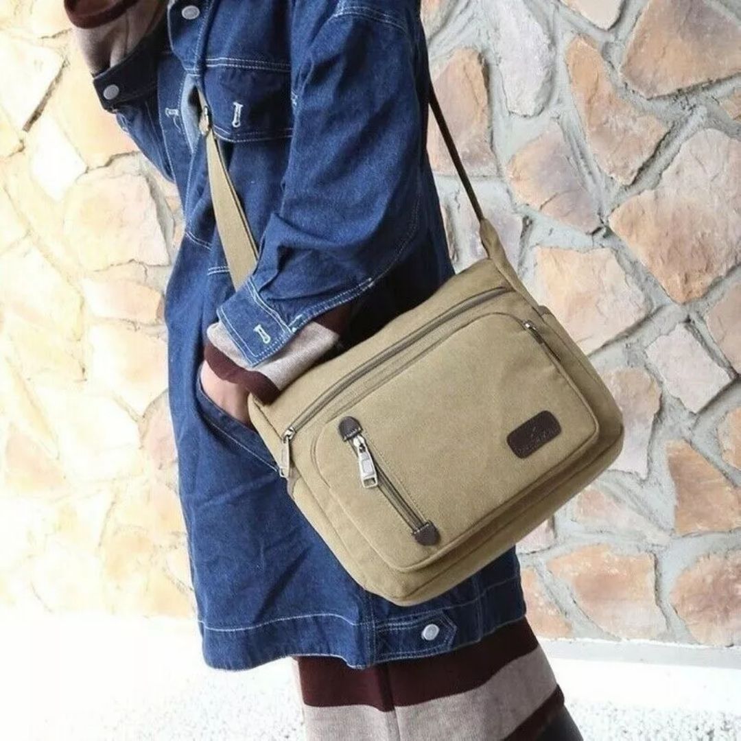 Khaki canvas Fitlybuy TravelPro shoulder bag with zip pockets, worn by a person in a denim jacket against a stone wall.
