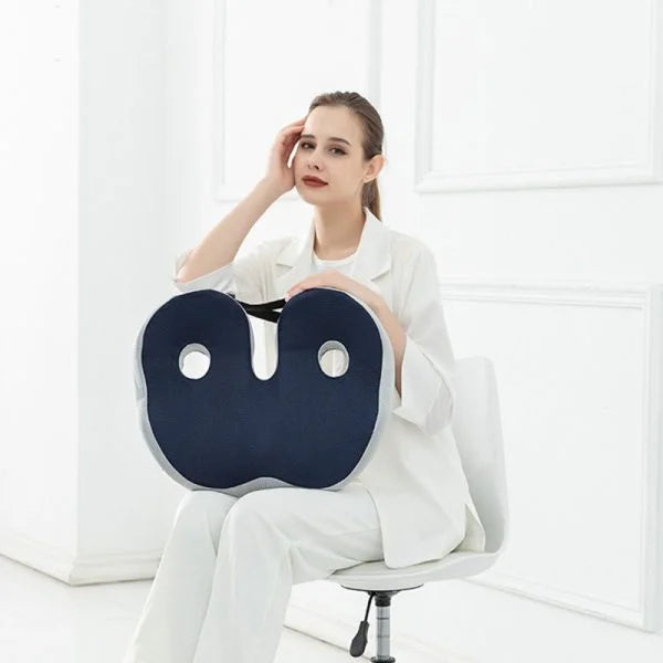 Woman holds a dark blue, ergonomic U-shaped sciatica relief seat cushion with cutouts for tailbone and hip support.
