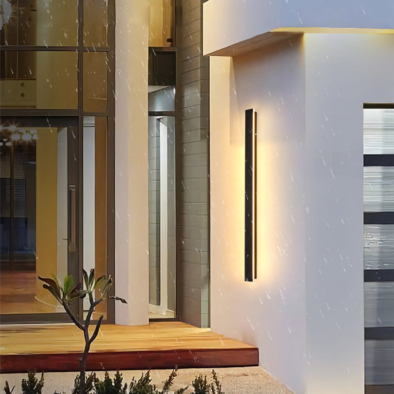 Fitlybuy slim black waterproof LED wall light illuminating a modern house exterior during rain.