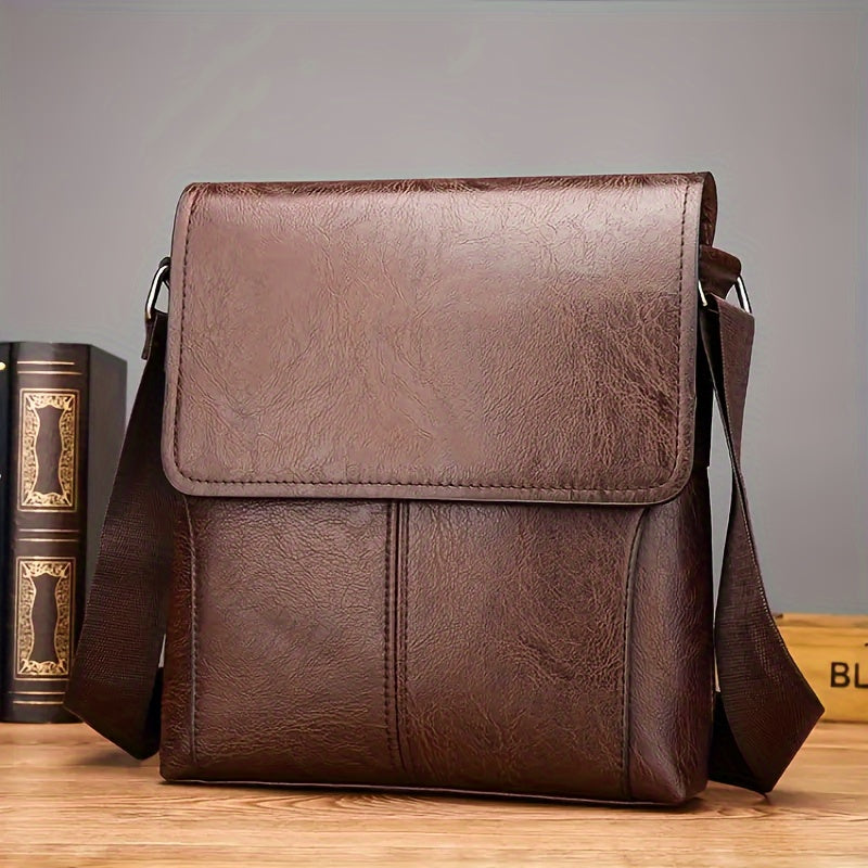 Brown vintage-style PU leather shoulder bag with flap closure and adjustable strap on a desk next to books.