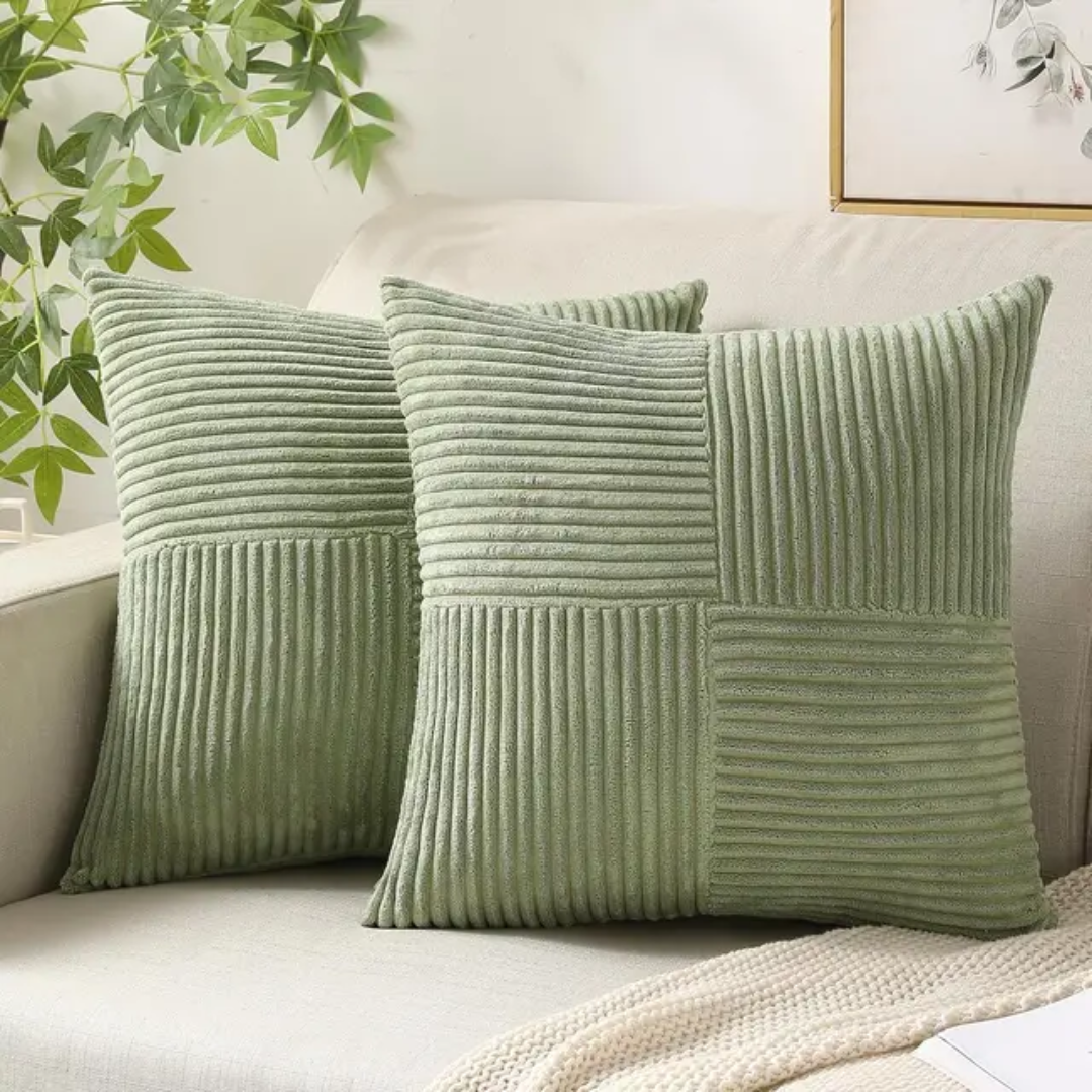 Two sage green corduroy decorative cushions with a textured panel design, displayed on a cream sofa.