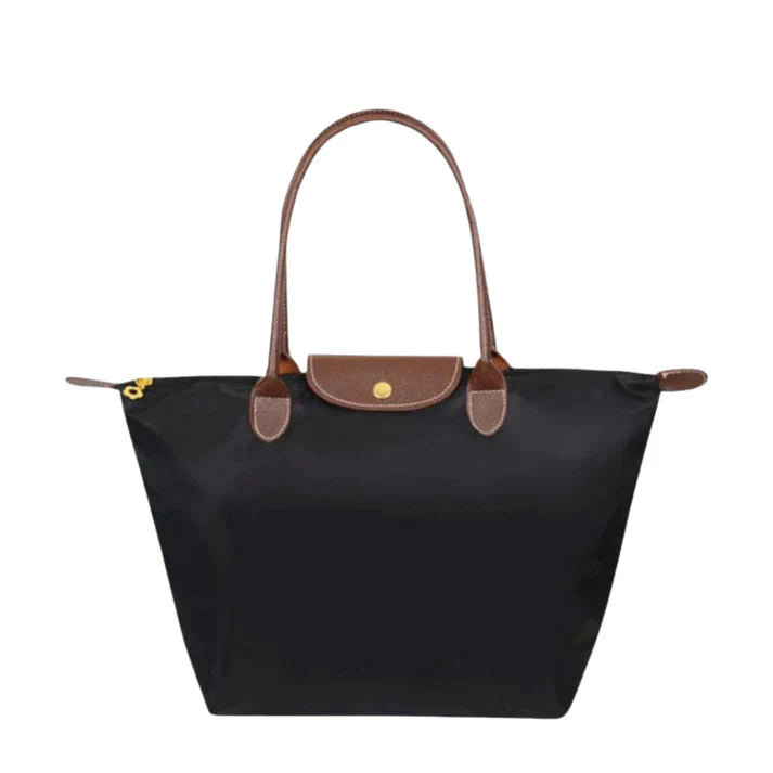 Black nylon tote handbag with brown leather handles, a gold-tone snap closure flap, and a zipper on a white background.