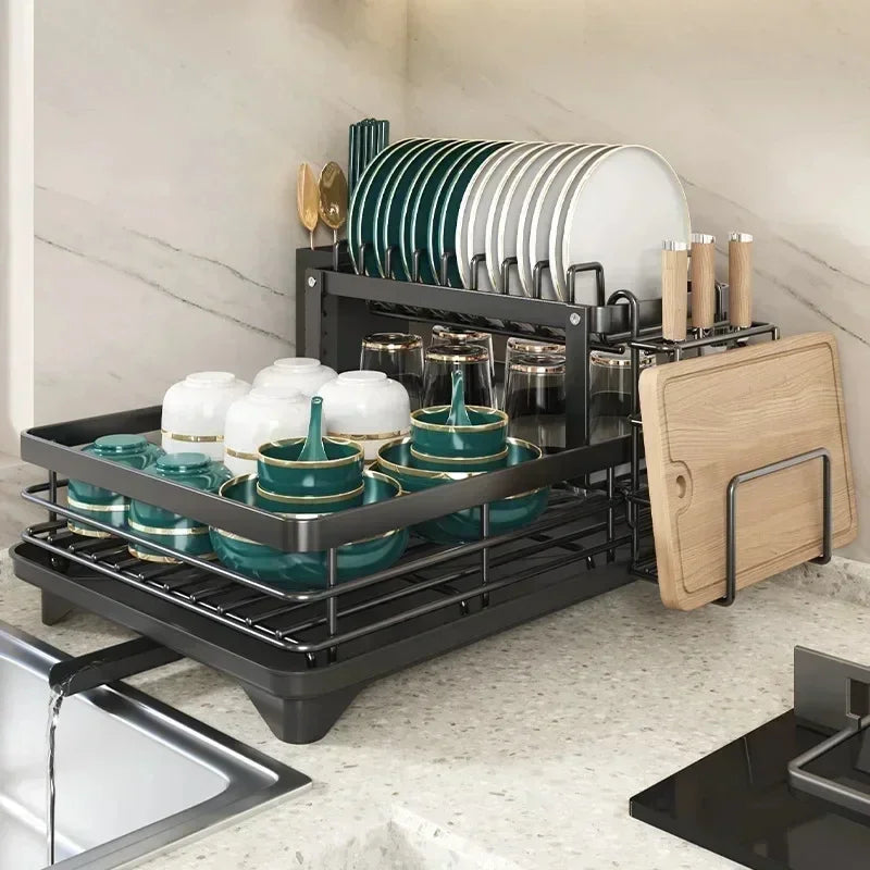 Fitlybuy black adjustable 2-tier dish drying rack holding plates, bowls, and a cutting board next to a kitchen sink.