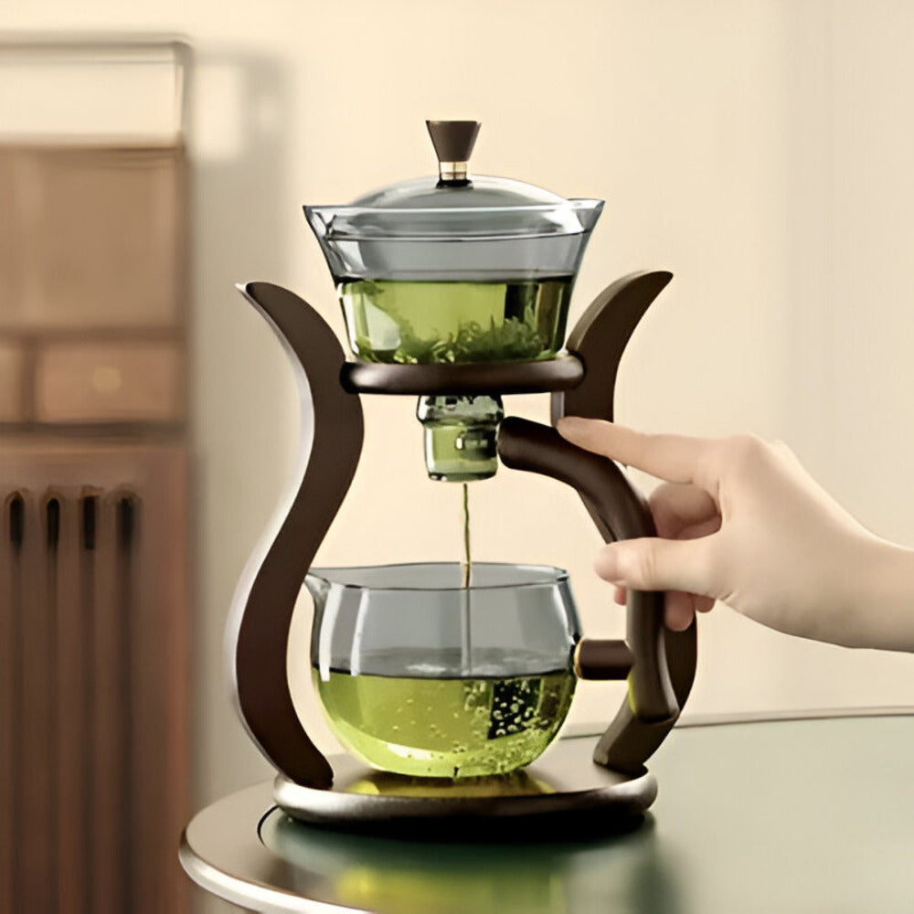 Fitlybuy artisan magnetic glass teapot with wooden stand, infusing green tea into a glass carafe on a table.