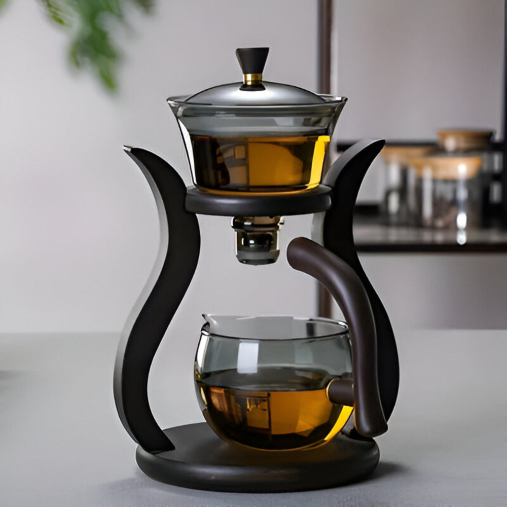 Artisan magnetic glass teapot set with infuser on a dark wooden stand, containing amber tea in a modern kitchen.