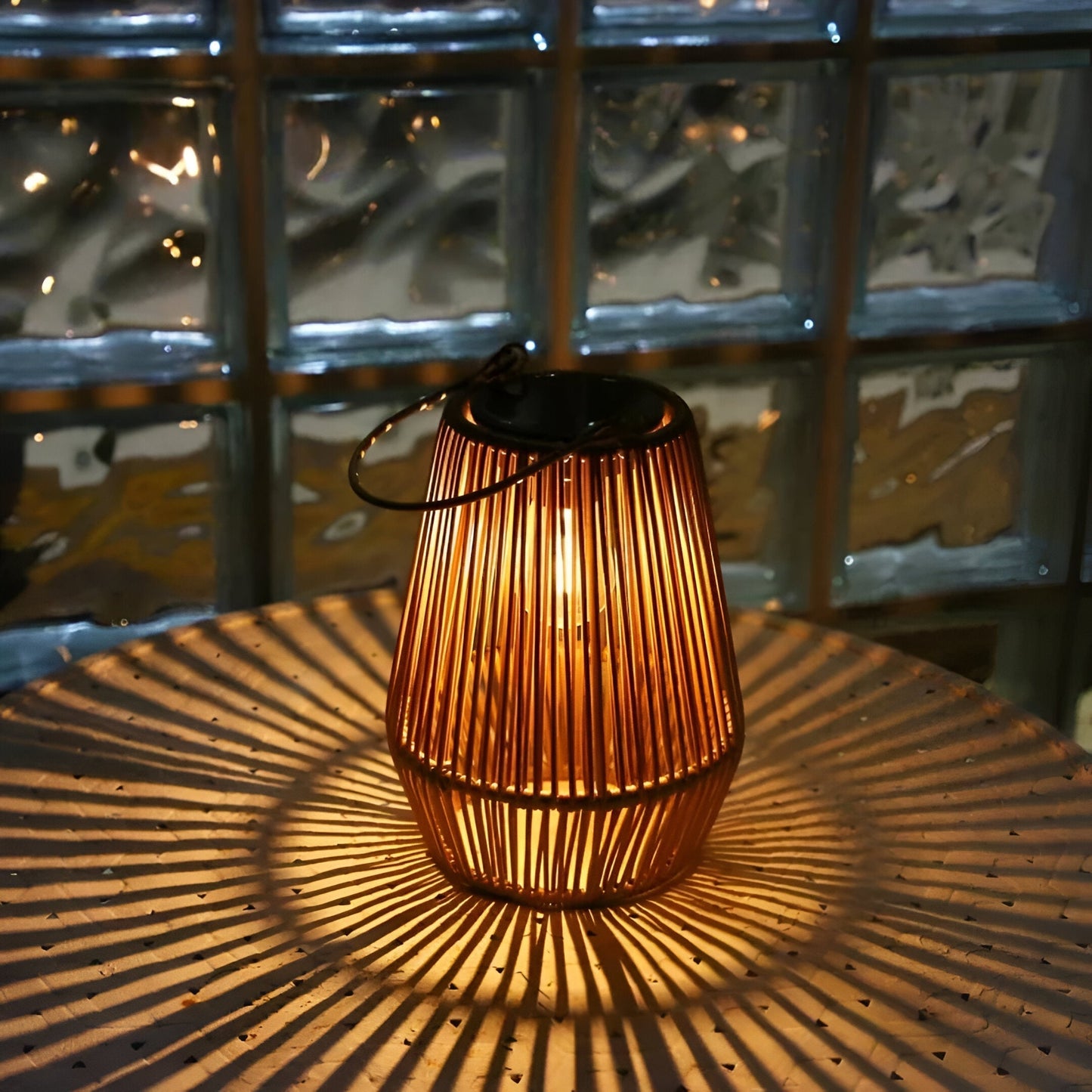 Fitlybuy bamboo solar garden lantern glows on a table, casting radial light patterns against a glass block background.