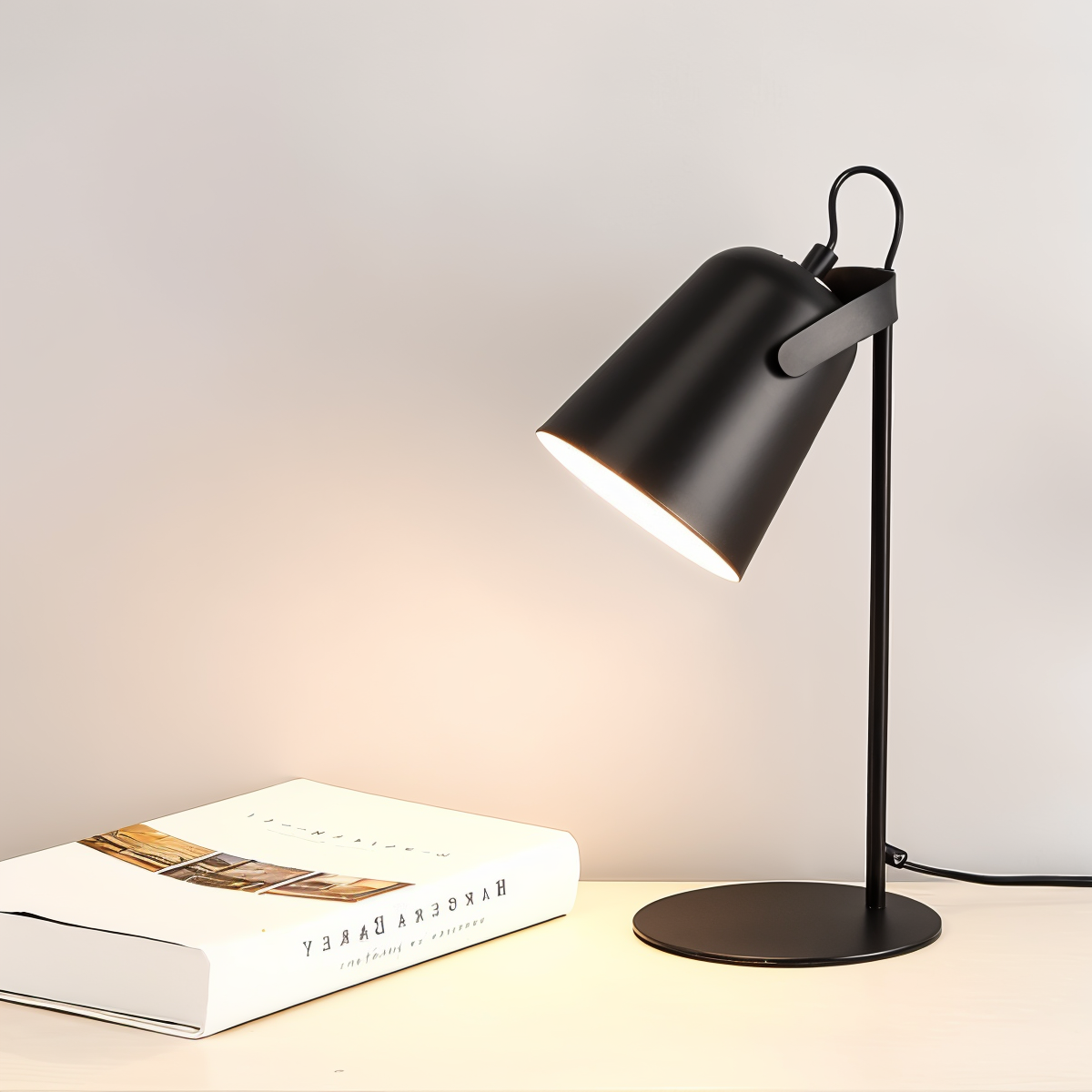 Matte black adjustable desk lamp with warm light, placed on a surface next to a white book against a neutral background.