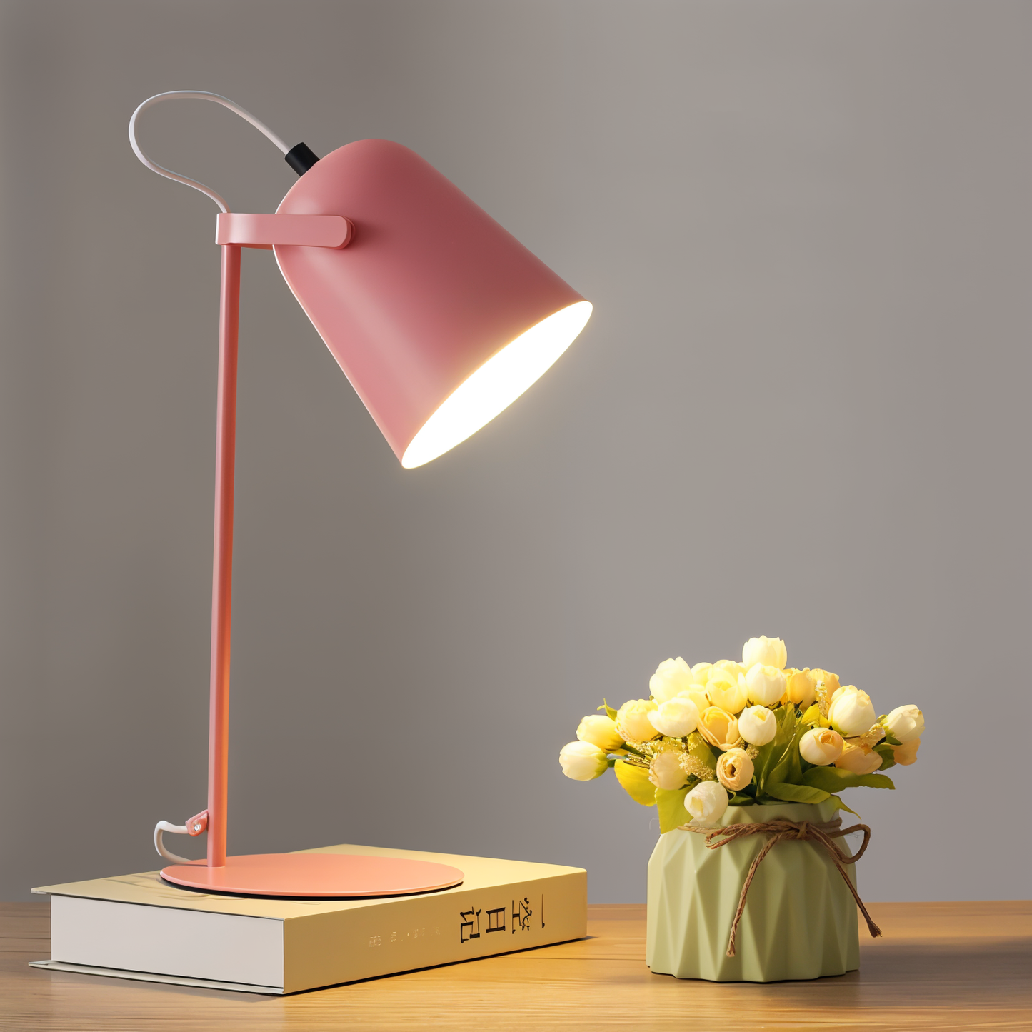 Fitlybuy pink Macaron desk lamp with adjustable head, illuminating a book and a small vase of flowers on a desk.