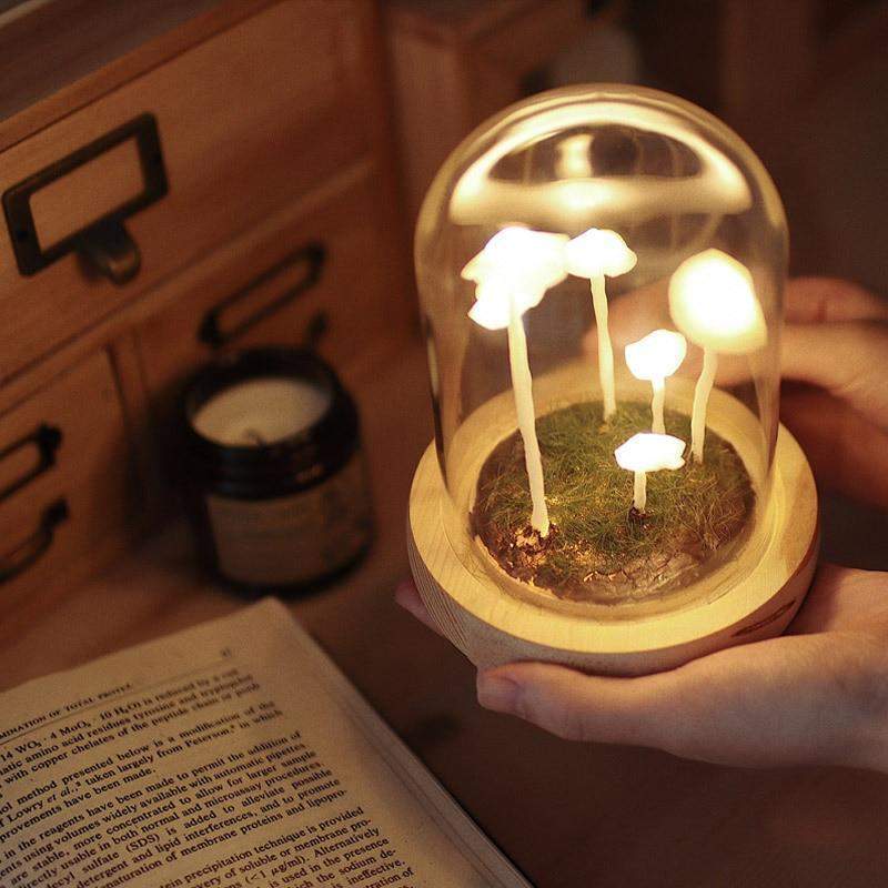 Fitlybuy DIY mushroom glass lamp with glowing white lights on a mossy base, held by hands over an open book.