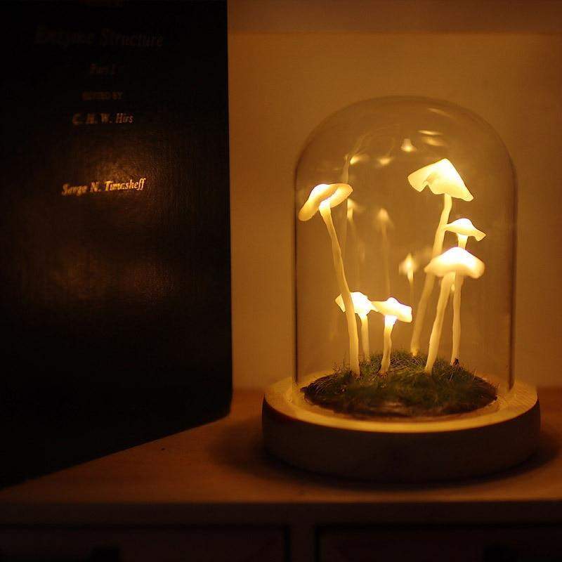 Fitlybuy Enchanted Mushroom DIY glass dome lamp with glowing white mushrooms on a wooden base next to a book.