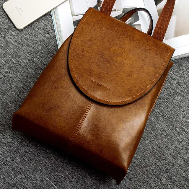 Fitlybuy brown leather backpack with a flap cover and fabric straps, resting on a textured gray surface.