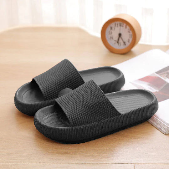 Fitlybuy dark grey Cloud Slides with textured, thick-sole ComfortFoam cushioning on a wooden desk with a clock.
