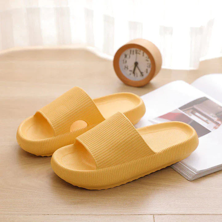 Yellow Fitlybuy Cloud Slides with ComfortFoam sole, featuring a textured upper on a wooden table with a clock and book.