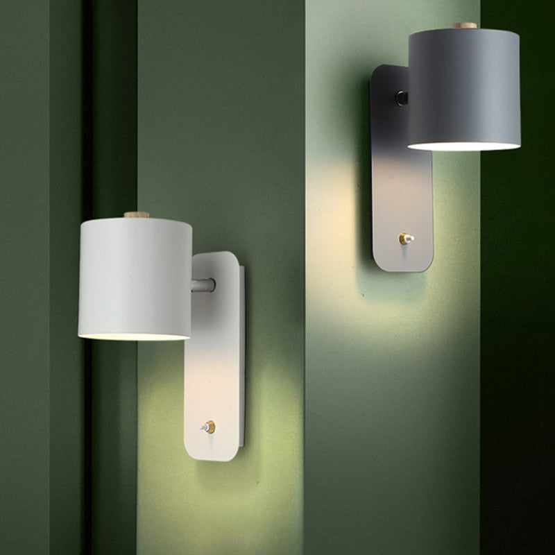White and grey modern LED wall lights with integrated switches mounted on a green wall.