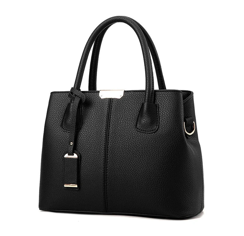 Black pebbled PU leather handbag with gold-tone hardware, top handles, and a detachable luggage tag against white.