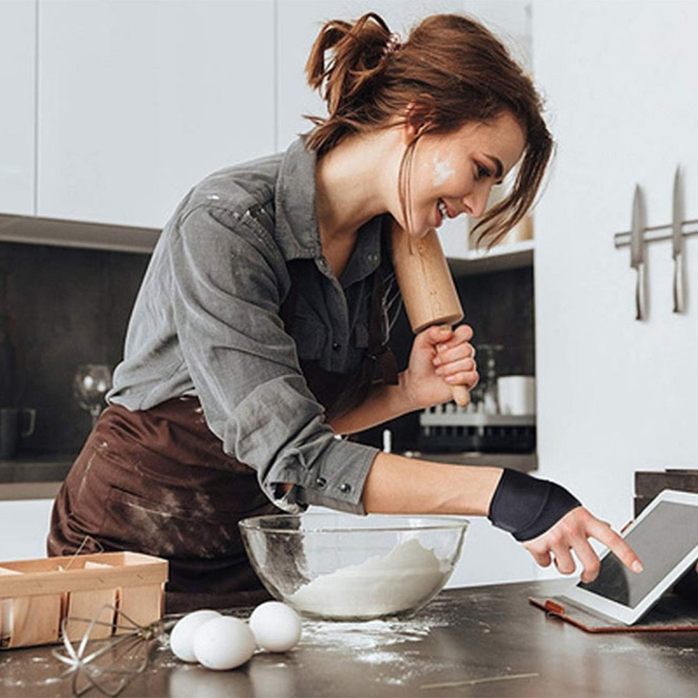 Woman wearing black Fitlybuy wrist brace while baking in a kitchen, using a tablet near a bowl of flour.