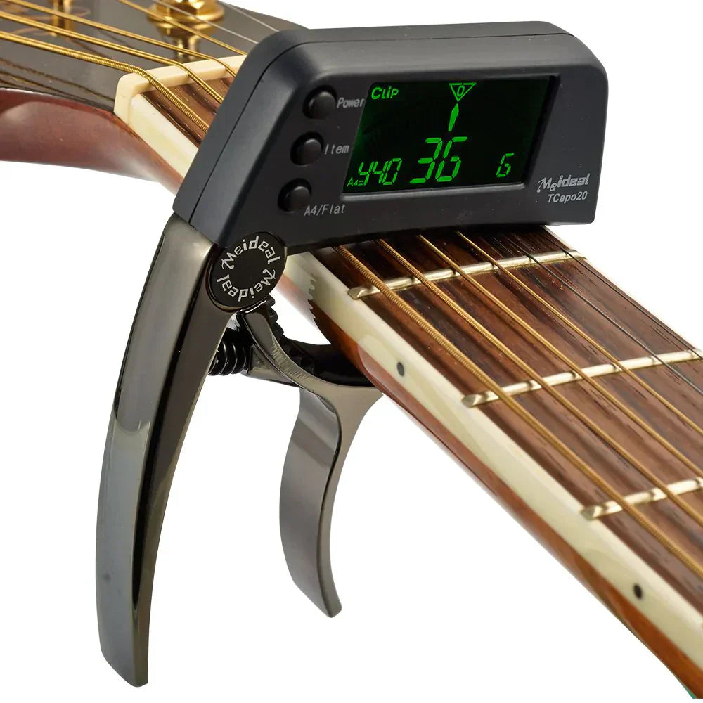 Black 2-in-1 guitar capo and digital tuner with a green-lit LCD screen attached to an acoustic guitar neck.