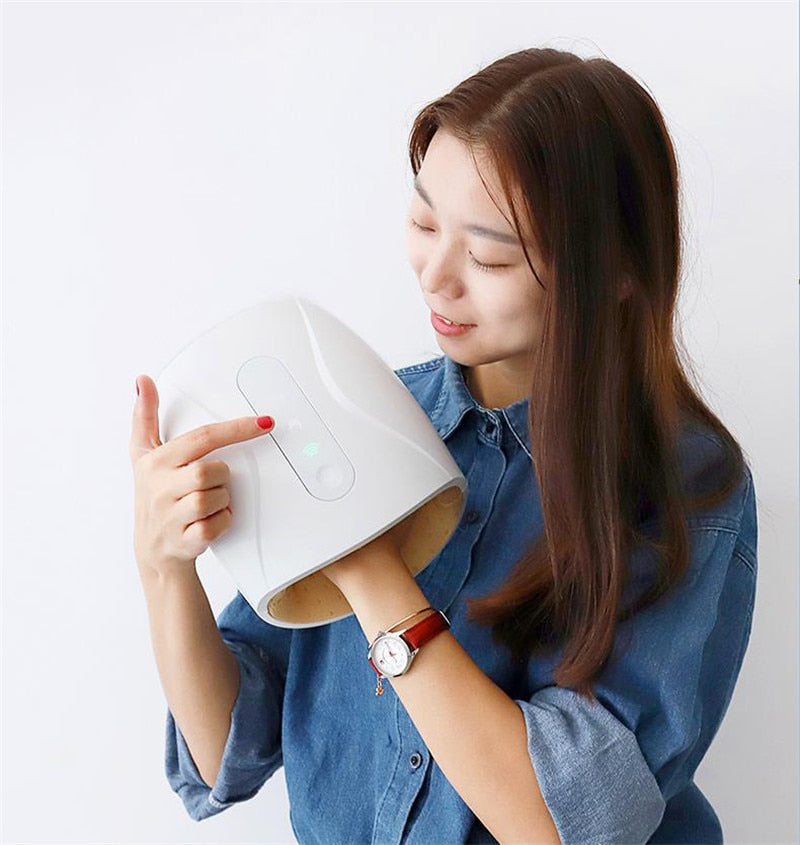 Woman using a white Fitlybuy deluxe hand massager with heat and air pressure features, touching the control panel.