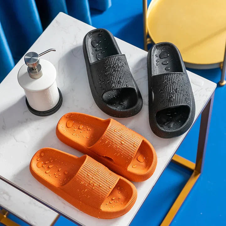 Fitlybuy Cloud Slides in black and orange on a white marble table next to a soap dispenser, featuring textured cushioning.