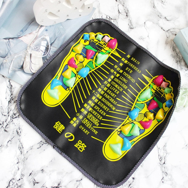 Black Fitlybuy reflexology mat with colorful stone pressure points and labeled foot acupuncture charts on white marble.