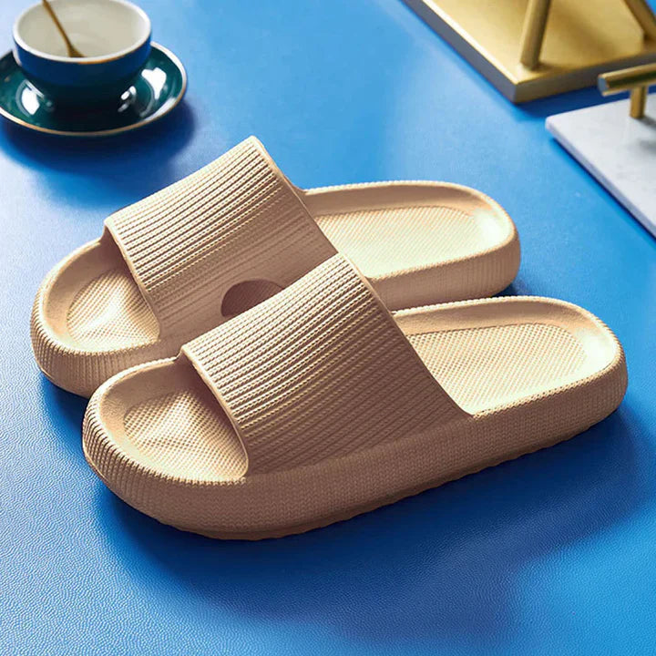 Beige Fitlybuy Cloud Slides with ComfortFoam cushioning, featuring a textured, thick-sole design on a blue surface.