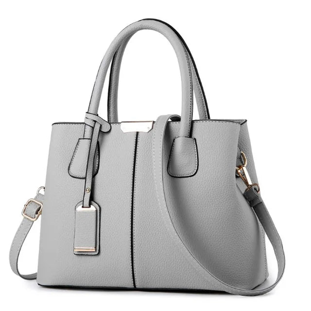 Light grey PU leather handbag with dual handles, detachable shoulder strap, and gold metal accents on a white background.