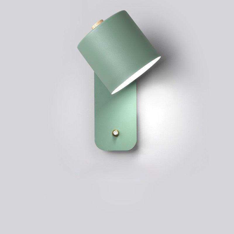 Sage green modern cylindrical LED wall light with wooden accent and integrated brass smart switch on a gray background.