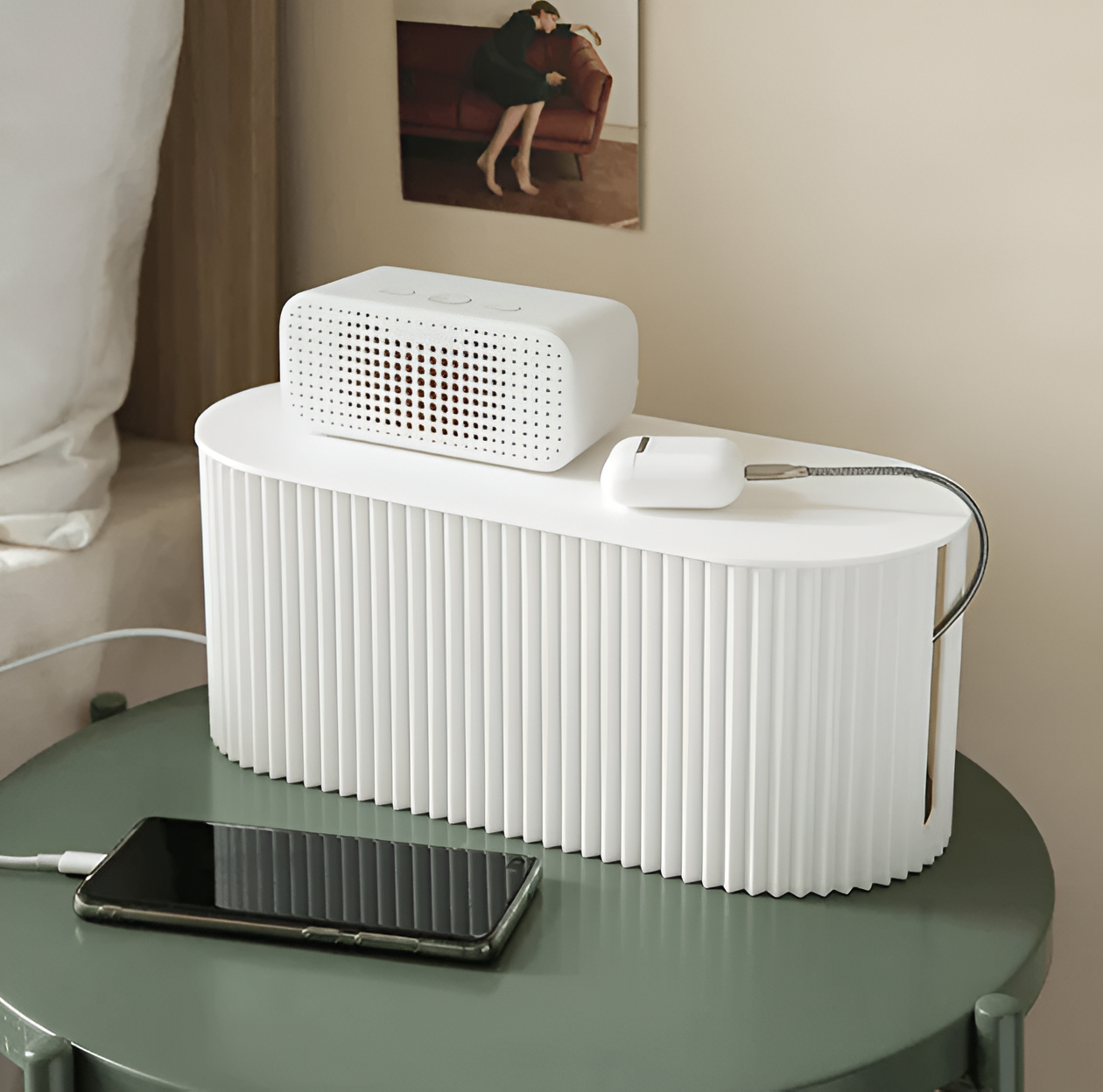 White ribbed Fitlybuy cable organizer box on a green nightstand, holding a speaker and charging earbuds.
